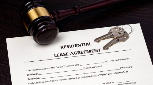 A residential lease agreement contract on a table with a gavel and keys laying on the document.