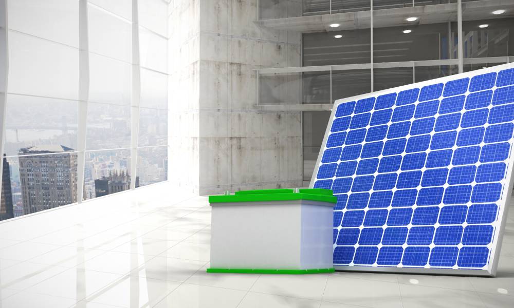 A solar panel connected to a green battery sitting inside of an office with large windows and marble floors.