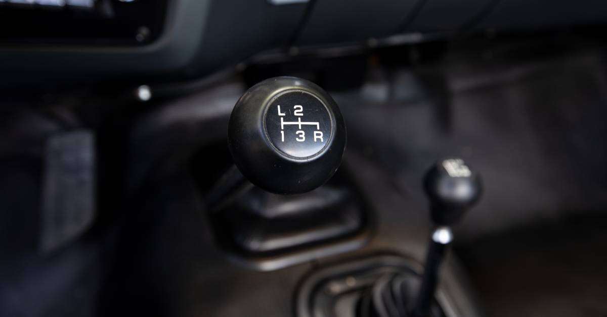 A black manual shift stick for a truck features the gears listed on the top in white. A radio sits near the shift stick.